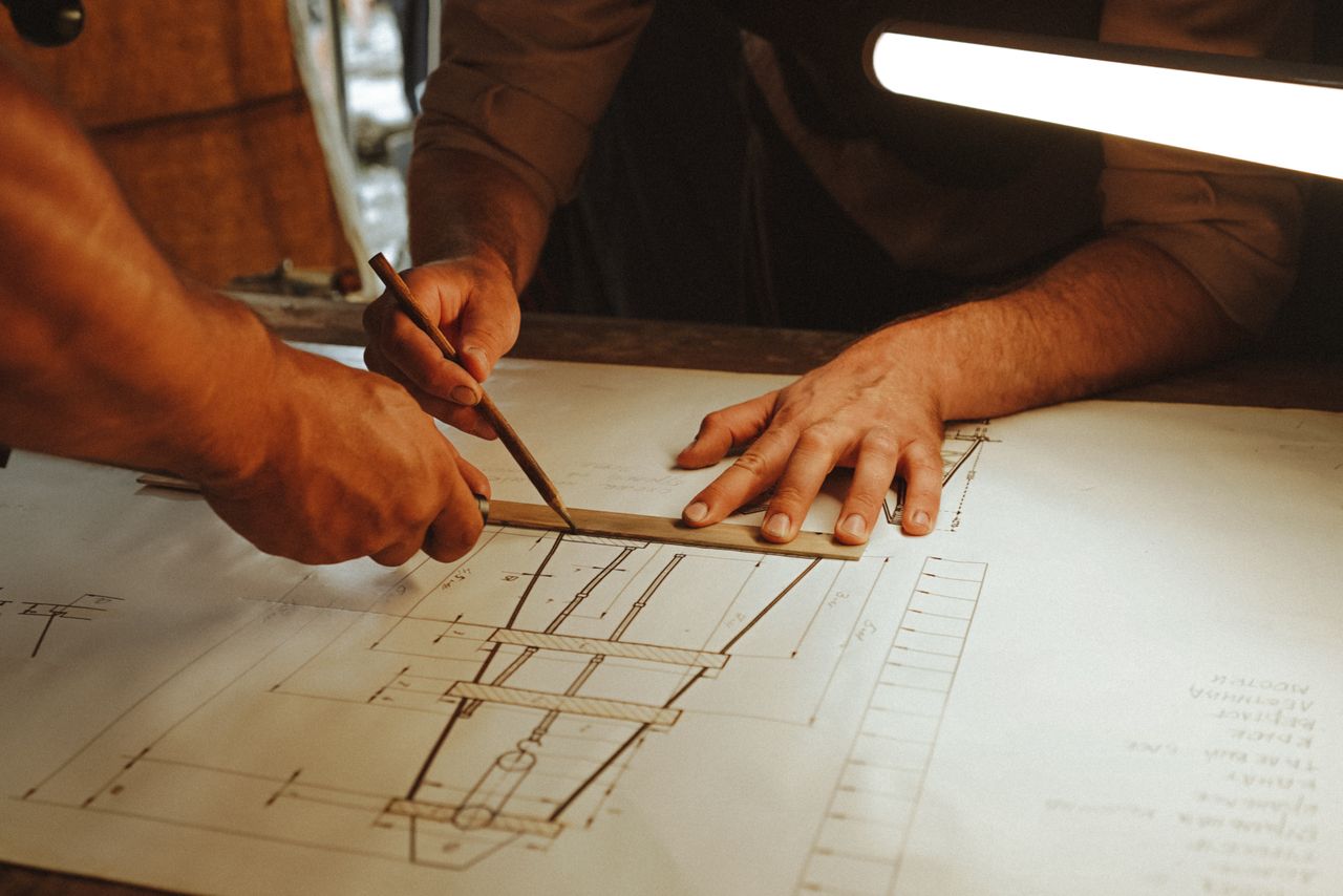 Two architects working together on a blueprint with precision tools under soft lighting.
