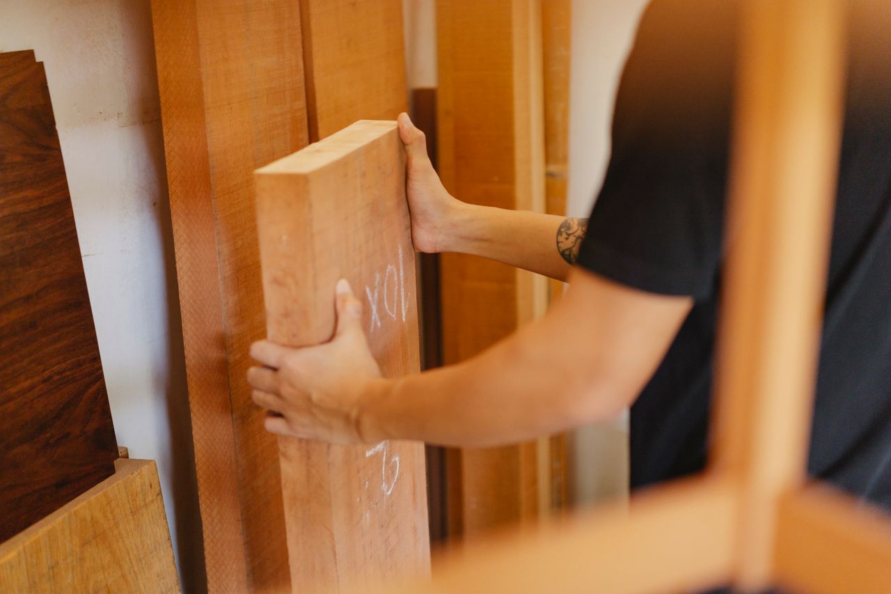 About Side view of crop anonymous joiner choosing wooden plank from assortment of timber in workshop